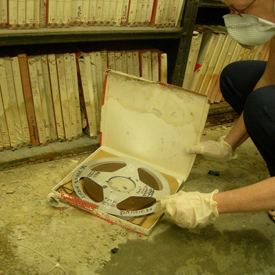 Exposed magnetic data tape reel in soiled, damp original box with mold growth