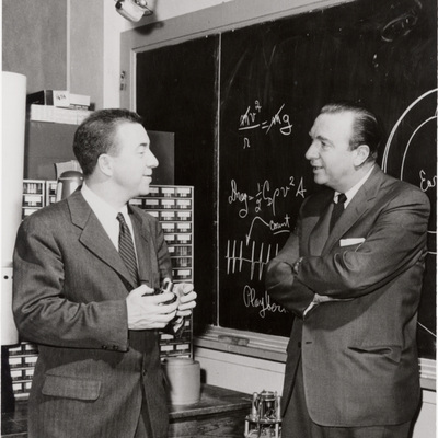 James Van Allen talking with Walter Cronkite in front of a chalk bord with equations and diagrams on it