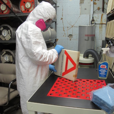 Preservationist in full hazard material suit and mask examining data tape reels